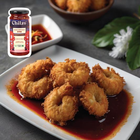 A plate of crispy coconut shrimp drizzled with vibrant sweet chilli sauce, garnished with fresh cilantro and lime wedges.