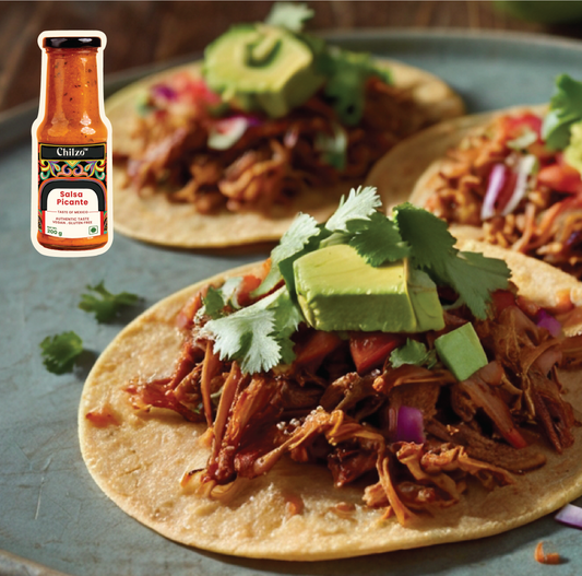 Shrimp tinga tostadas topped with creamy avocado slices and vibrant salsa picante, garnished with fresh cilantro and lime wedges, served on a rustic plate.