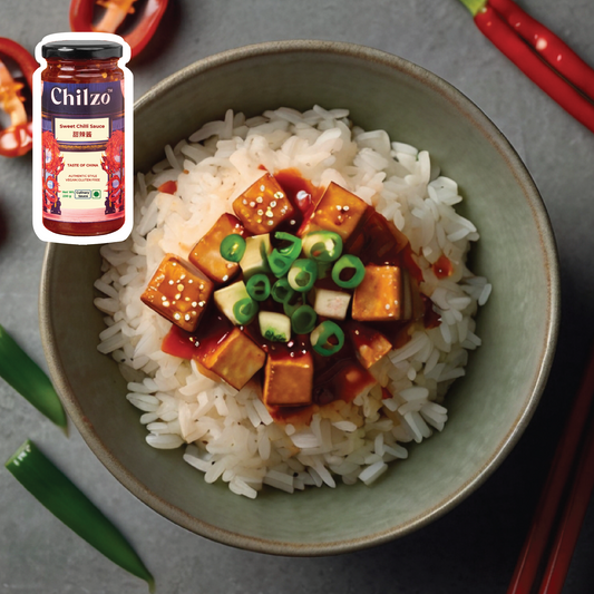 A bowl with rice, crispy tofu, colourful veggies, and Chilzo's sweet chilli sauce. 